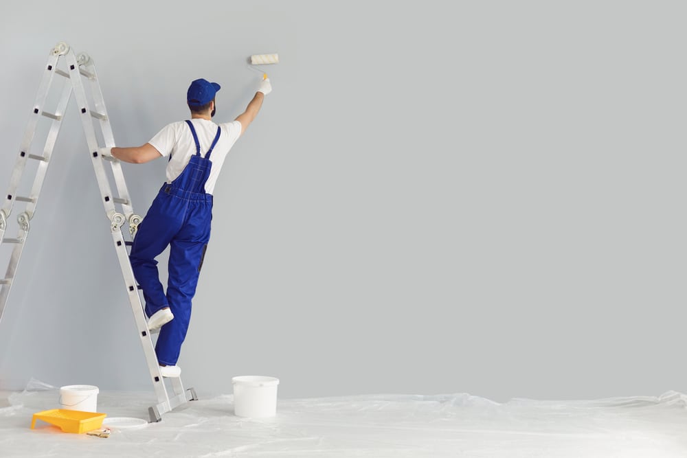 Painter on ladder with paintbrush painting wall