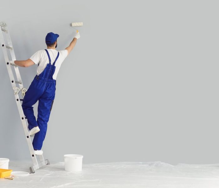 Painter on ladder with paintbrush painting wall